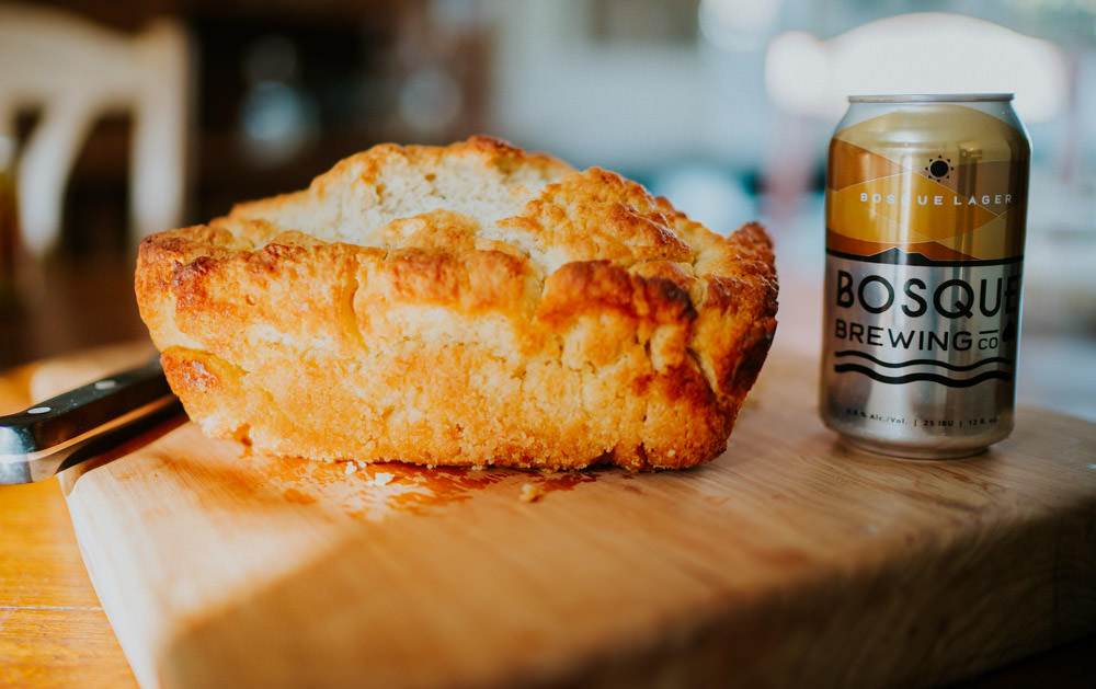 A loaf of bread with a can of beer next to it on a cutting board.